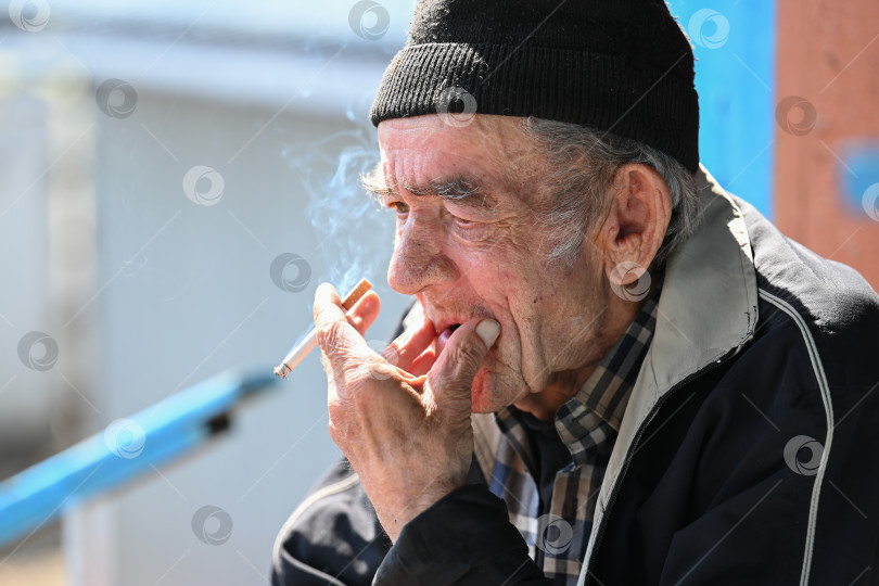 Скачать Задумчивый русский пожилой мужчина 77 лет, курящий сигарету с грустным выражением лица на улице в бедном районе в России фотосток Ozero