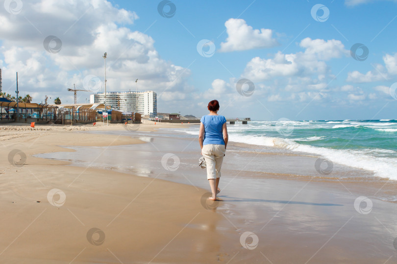 Скачать Бат-Ям, Израиль - 14 июля 2014 года. Стройная пожилая леди прогуливается по песчаному пляжу фотосток Ozero