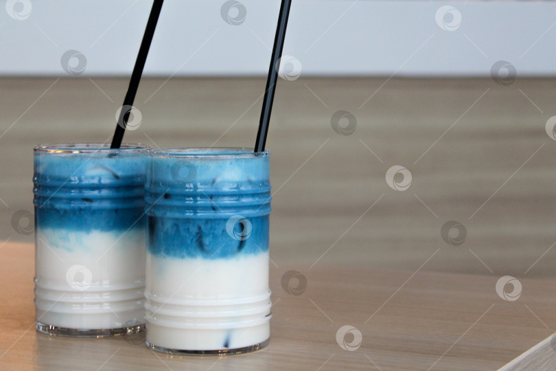Скачать Два стакана горохового латте со льдом. Слоеный коктейль из голубого чая с молоком на деревянном столе с черной соломинкой и льдом фотосток Ozero