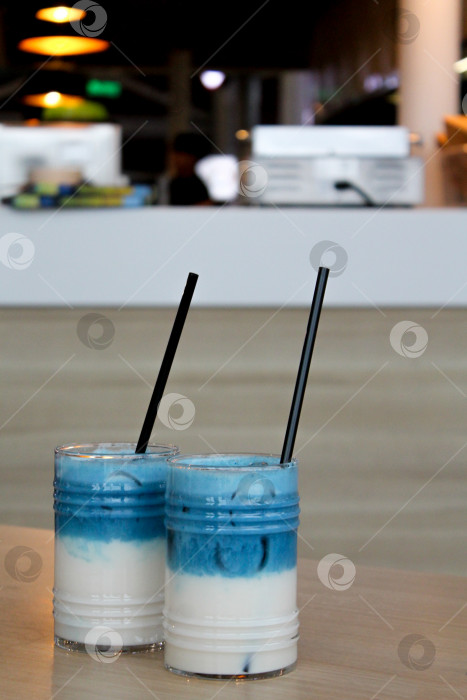 Скачать Два стакана горохового латте со льдом. Слоеный коктейль из голубого чая с молоком на деревянном столе с черной соломинкой и льдом фотосток Ozero