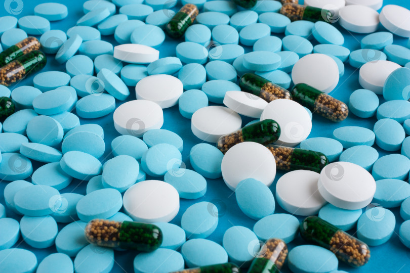 Скачать Белые и светло-голубые таблетки, зеленые капсулы на синем фоне. Медицина и здоровье фотосток Ozero