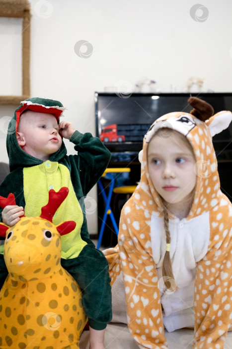Скачать Двое детей, одетых в костюмы животных, сидят на покрытом ковром полу фотосток Ozero