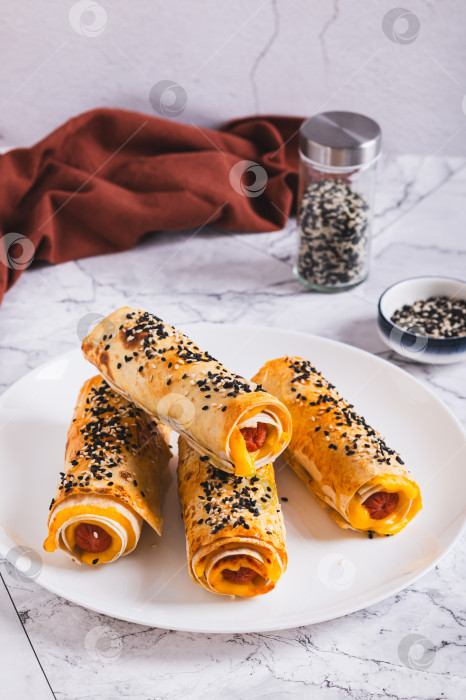 Скачать Роллы на гриле с сосисками, сыром, лавашом и кунжутом на тарелке на столе, вид сверху фотосток Ozero