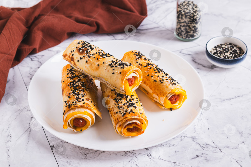 Скачать Роллы на гриле с сосисками, сыром, лавашом и кунжутом на тарелке на столе фотосток Ozero