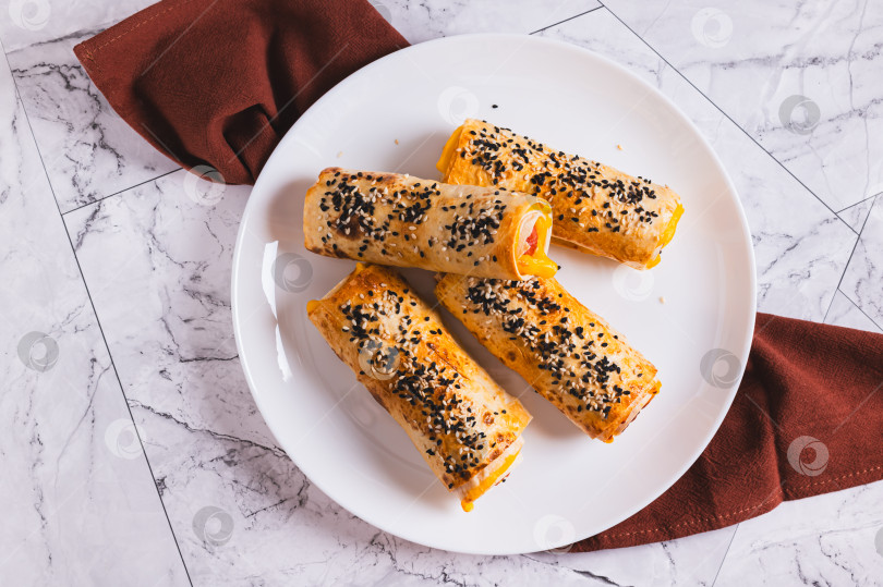 Скачать Крупный план сосисок с сыром, запеченных в лаваше, на тарелке на столе, вид сверху фотосток Ozero