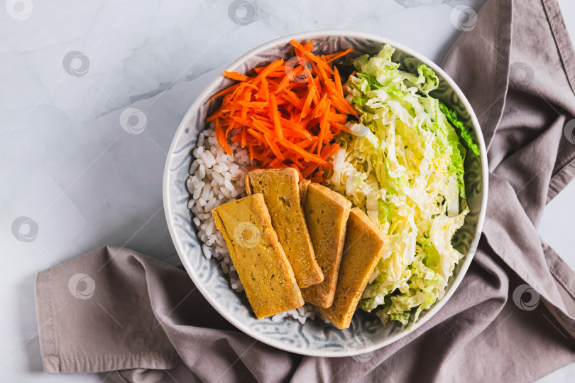 Скачать Тарелка риса с жареным тофу, китайской капустой и морковью крупным планом на столе, вид сверху фотосток Ozero