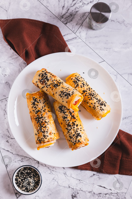 Скачать Роллы на гриле с колбасками, сыром, лавашом и кунжутом на тарелке, установленной на столешнице, в вертикальном положении фотосток Ozero