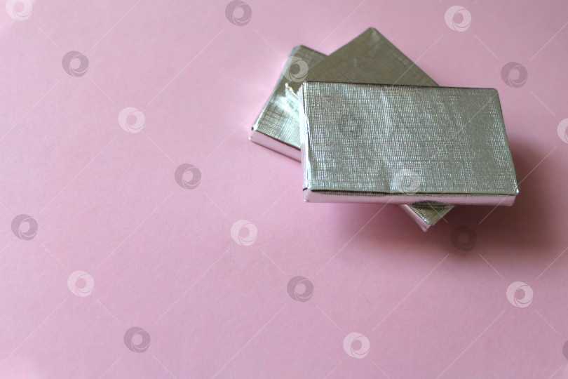 Скачать Горка шоколадных конфет, завернутых в серебряную фольгу, выделяющуюся на розовой поверхности фотосток Ozero