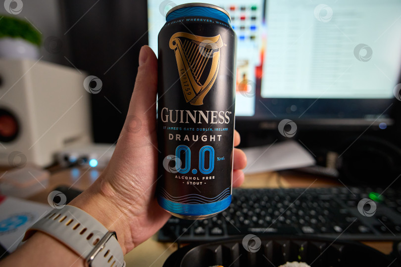 Скачать Тюмень, Россия - 15 февраля 2026 года: Банка пива Guinness стоит на столе рядом с компьютером с документами фотосток Ozero