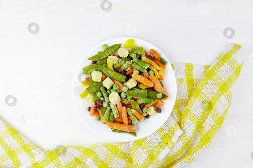 Скачать Замороженные овощи на белой тарелке: кукуруза, стручковая фасоль, перец, зеленый горошек и морковь. Вид сверху с пространством для копирования. фотосток Ozero