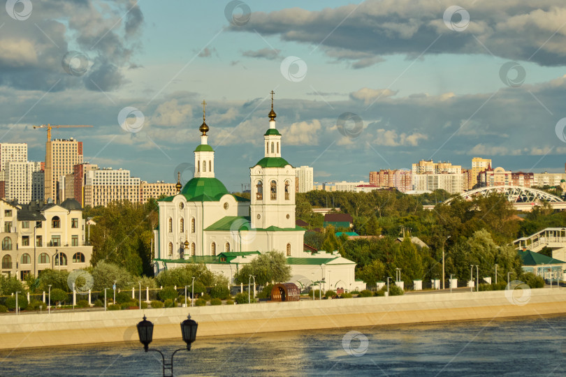Скачать Тюмень, Россия - 6 сентября 2026 года: Русская православная Свято-Воздвиженская церковь с зелеными куполами, стоящая на гранитной набережной реки Тура на фоне современного города. фотосток Ozero