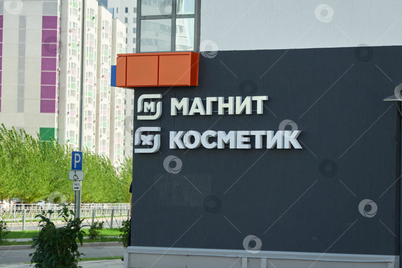 Скачать Тюмень, Россия - 6 сентября 2026 года: Вывеска магазина "Магнит Косметик" с белым кириллическим логотипом на темно-серой стене современного жилого дома фотосток Ozero