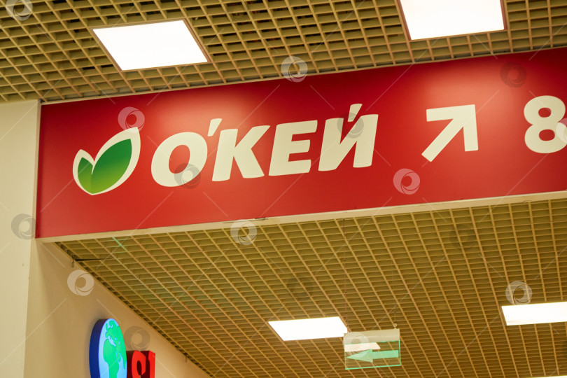 Скачать Тюмень, Россия - 6 сентября 2026 года: Вид под низким углом на внутреннюю вывеску гипермаркета red OKEY с белой стрелкой, указывающей в сторону касс фотосток Ozero