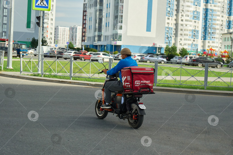 Скачать Тюмень, Россия - 6 сентября 2026 года: Курьер отдела доставки "Магнит" катается на электрическом самокате фотосток Ozero