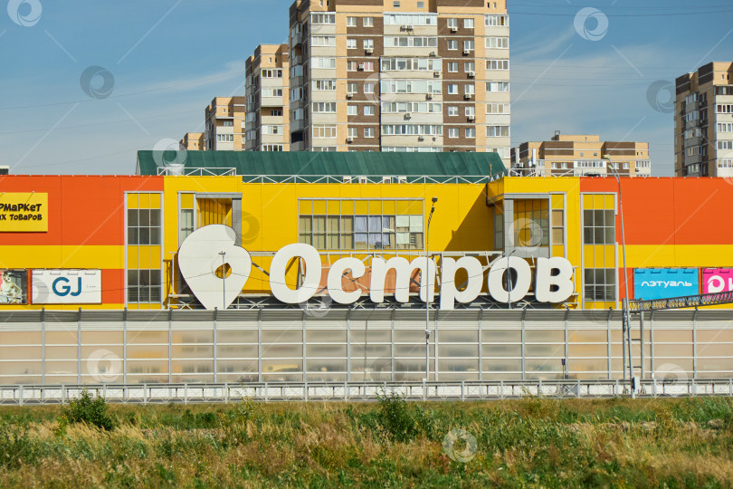 Скачать Тюмень, Россия - 6 сентября 2026 года: вдалеке виден яркий желто-оранжевый фасад торгового центра "Остров" на фоне голубого неба. фотосток Ozero