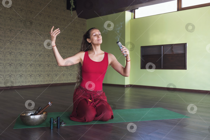 Скачать Женщина, практикующая йогу, занимающаяся медитацией с благовониями, сидит на коврике в комнате фотосток Ozero