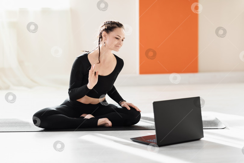 Скачать Женщина-универсальный тренер по йоге приветствует учеников за ноутбуком перед началом онлайн-тренировки фотосток Ozero
