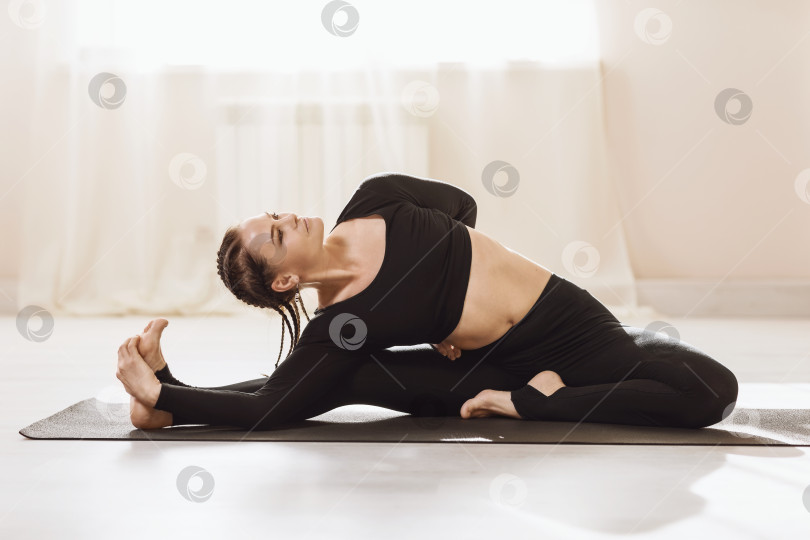 Скачать Женщина в спортивной одежде, занимающаяся йогой, сидя на коврике, выполняет упражнение Паривритта Джану ширшасана, поза "голова к коленям" фотосток Ozero