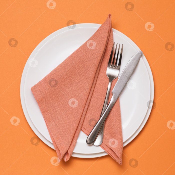 Скачать Свернутая текстильная салфетка в керамической тарелке и столовые приборы на оранжевом фоне, вид сверху фотосток Ozero