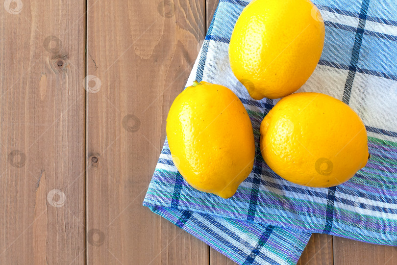 Скачать три свежих лимона на деревянном столе. рядом с ним лежит хлопчатобумажное кухонное полотенце фотосток Ozero