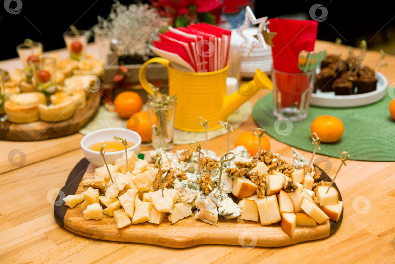 Скачать Деревянная доска с кусочками сыра, меда, грецких орехов. Сыр с плесенью (Горгонзола), пармезан, твердый копченый сыр на праздничный стол с мандаринами. фотосток Ozero