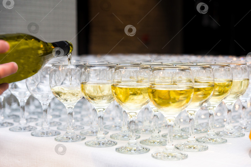 Скачать Бокалы наполняются алкогольными напитками, рука официанта наливает белое вино из бутылки фотосток Ozero