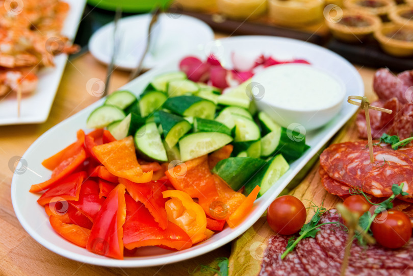 Скачать Тарелка со свежими нарезанными овощами: красным болгарским перцем, огурцом, редиской и миска с соусом фотосток Ozero