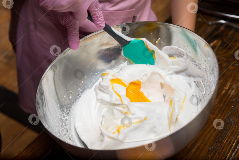 Скачать Смешайте яичный желток со взбитыми белками акриловой лопаткой в металлической миске фотосток Ozero
