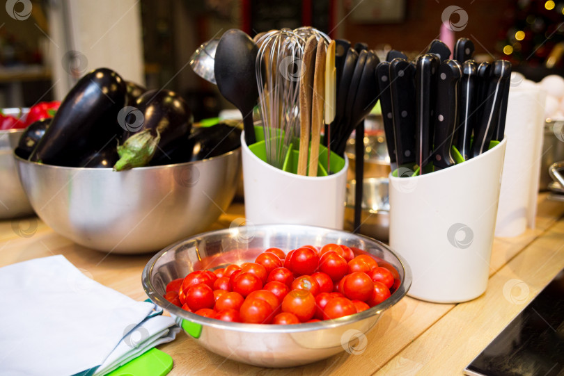Скачать Сырые помидоры черри, сырые баклажаны в металлических мисках. Сырые продукты перед приготовлением. Набор кухонных принадлежностей и ножей. фотосток Ozero