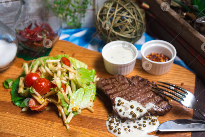 Скачать Кусок говядины на гриле с соусом из зеленого перца на деревянной доске с салатом фотосток Ozero