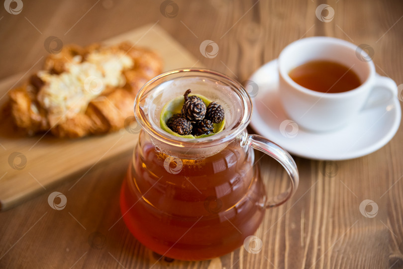 Скачать Завтрак в кафе. можжевеловый чай с лаймом подается в стеклянном графине, с чашкой горячего чая и круассаном с миндалем. фотосток Ozero
