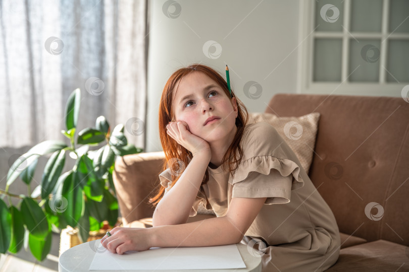 Скачать задумчивая симпатичная девушка с карандашом за ухом сидит на диване и думает о том, что бы нарисовать фотосток Ozero