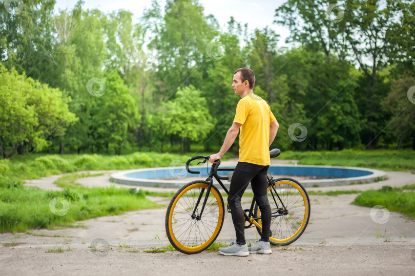 Скачать Молодой человек остановился отдохнуть со своим велосипедом в общественном парке. фотосток Ozero
