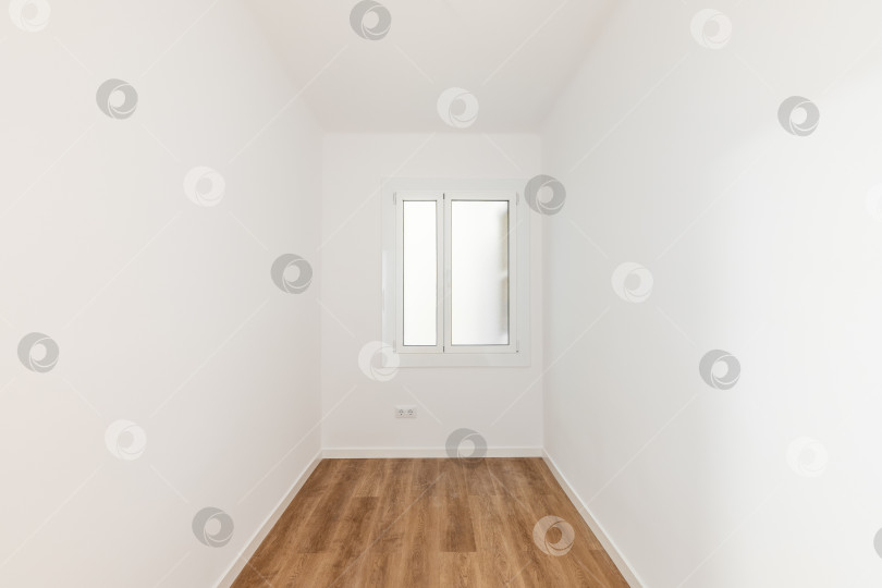 Скачать Пустая комната с ламинатным полом, недавно выкрашенными в белый цвет стенами и светлым окном с матовым стеклом. Концепция ремонта и строительства. фотосток Ozero