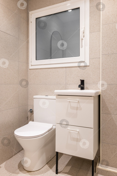 Скачать Часть ванной комнаты с унитазом, умывальником на деревянной мебели и стенами, выложенными бежевой плиткой фотосток Ozero