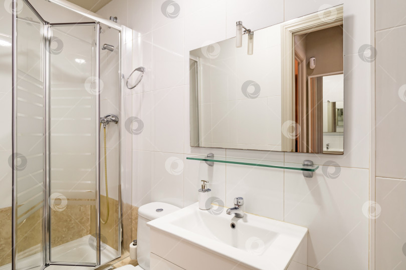 Скачать Ванная комната со светло-бежевыми стенами. В углу находится душевая кабина со стеклянными раздвижными дверцами. Туалетный столик с раковиной и белой мебелью и унитазом. фотосток Ozero