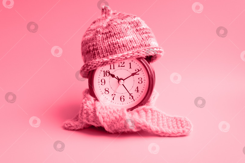 Скачать красный круглый будильник в вязаной шерстяной шапочке и шарфе красно-фиолетово-розового цвета. концепция зимнего времени. зимний сезон. уютно и тепло. аналоговое время 10:10. окрашен в viva magenta, трендовый цвет 2023 года. фотосток Ozero