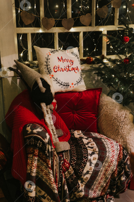 Скачать время Рождества и нового года. уютное мягкое кресло с удобным пледом и красной подушечкой и гномом ниссе возле украшенной рождественской елки. сезон зимних каникул дома фотосток Ozero