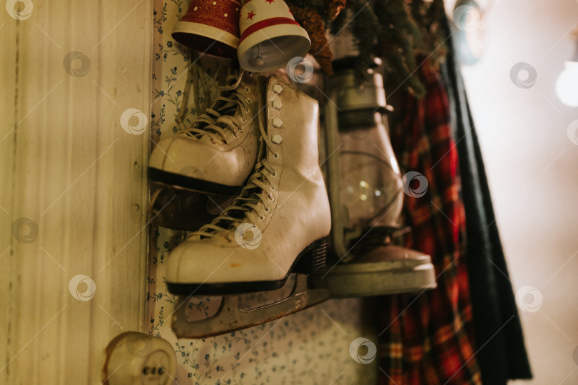 Скачать старинные женские фигурные коньки в стиле ретро висят на вешалке на стене вместе со старинной керосиновой лампой и рождественскими колокольчиками jingle bells. время Рождества и нового года. сезон зимних каникул дома фотосток Ozero