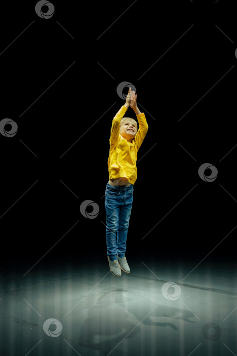 Скачать счастливый искренний маленький шестилетний малыш мальчик встает во весь рост подпрыгивает и хлопает в ладоши в студии освещенной бело желтым ярким светом фотосток Ozero