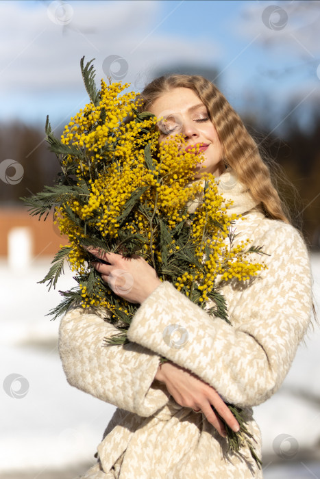 Скачать Молодая женщина стоит с букетом желтой мимозы и нюхает цветы. Концепция весеннего праздника - 8 марта, Пасха, Женский день фотосток Ozero