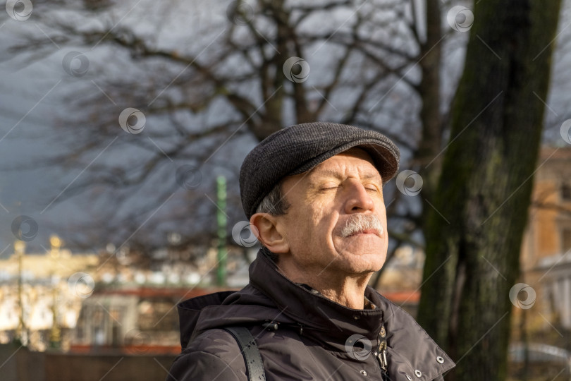 Скачать Взрослый мужчина пенсионного возраста поздней осенью стоит в парке и подставляет лицо солнечным лучам фотосток Ozero