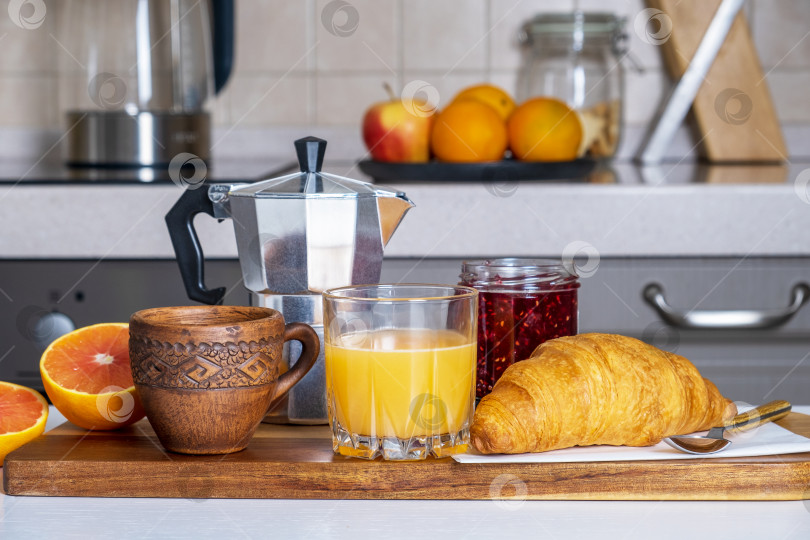 Скачать Завтрак из круассана, джема, чашки, стакана сока и кофеварки на кухонном столе фотосток Ozero