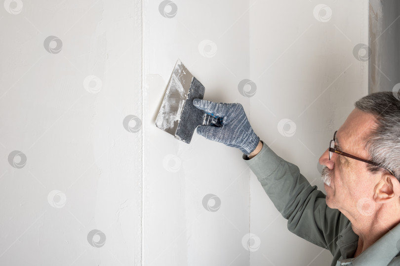 Скачать Взрослый мужчина выравнивает и зашпаклевывает углы в своем доме фотосток Ozero