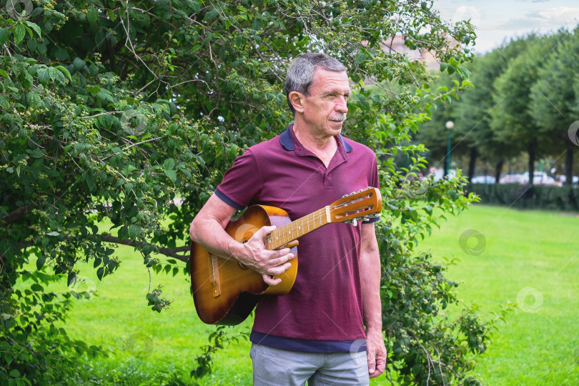 Скачать Взрослый мужчина стоит в городском парке летним вечером и держит акустическую гитару фотосток Ozero