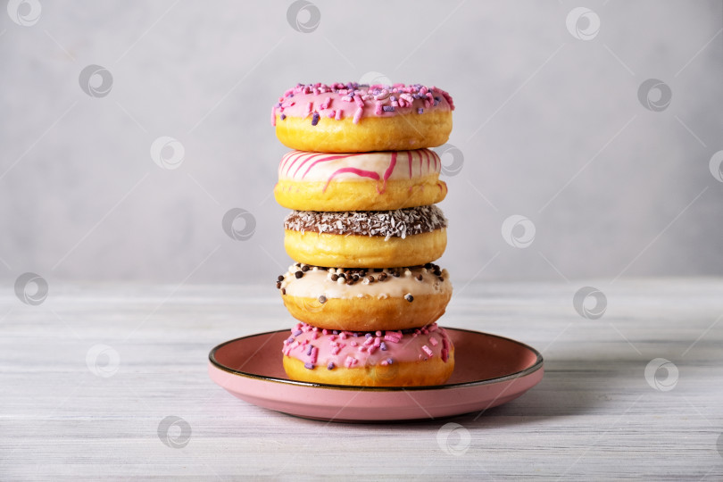 Скачать Стопка разноцветных пончиков на розовой керамической тарелке фотосток Ozero