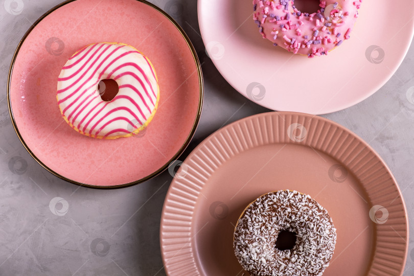 Скачать Три глазированных пончика лежат на высоких розовых тарелках фотосток Ozero