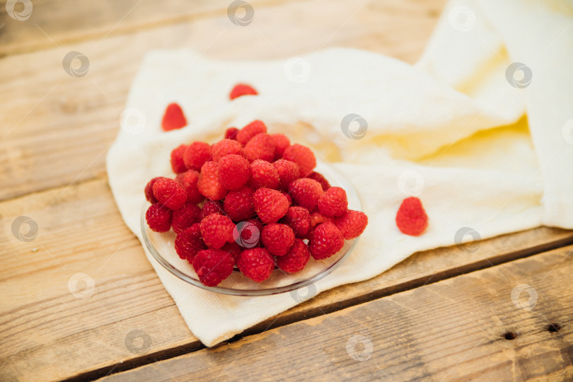 Скачать Плоды малины на маленьком блюдце, гроздь летних ягод на деревянном фоне. Летний фон. Сочная закуска или десерт. фотосток Ozero