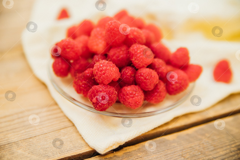 Скачать Плоды малины на маленьком блюдце, гроздь летних ягод на деревянном фоне. Летний фон. Сочная закуска или десерт. фотосток Ozero