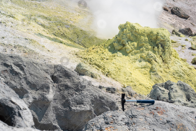Скачать геологический молоток в скале на фоне дымящейся фумаролы на склоне вулкана фотосток Ozero